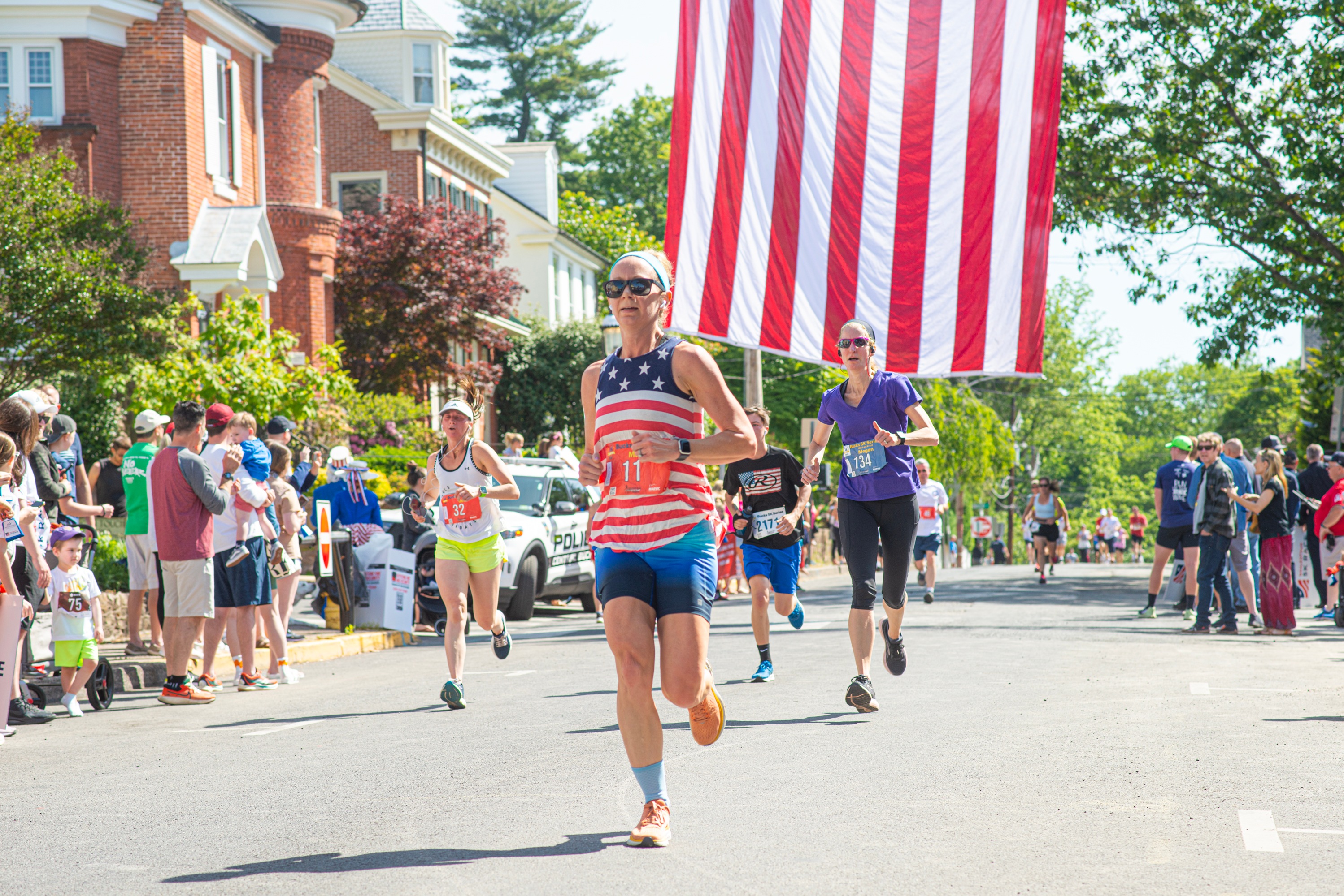 A runner in a stars-and-stripes tank leading down a historic downtown Doylestown street lined with cheering spectators
